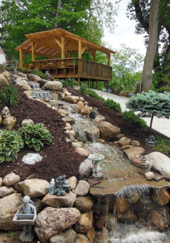 stone waterfall feature beside cement walkway with landscaping