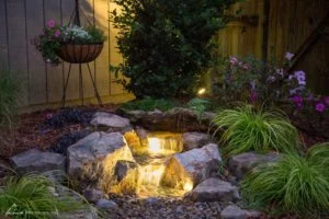 Illuminated garden waterfall with plants and flowers.